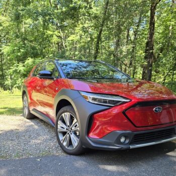 Sleek red Subaru Solterra electric SUV parked on gravel with lush green forest backdrop