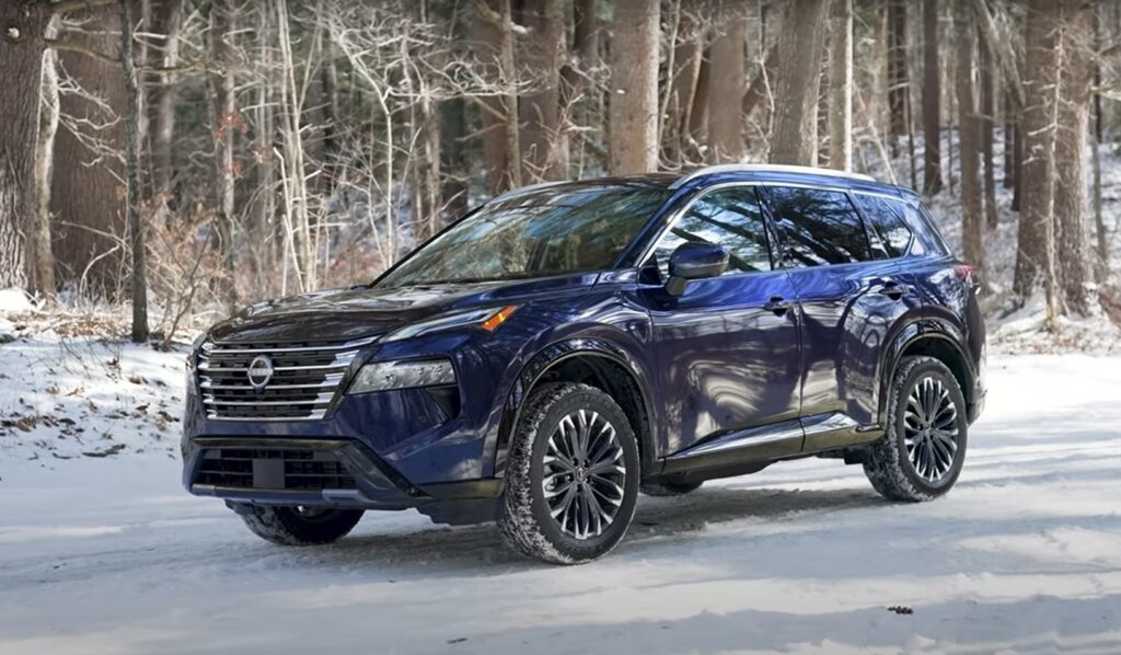Dark blue Nissan Rogue SUV parked on snowy forest road, winter tires gripping snow-covered ground amid bare trees