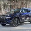 Dark blue 2025 Nissan Rogue SUV parked on snowy forest road, winter tires gripping snow-covered ground amid bare trees