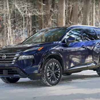 Dark blue 2025 Nissan Rogue SUV parked on snowy forest road, winter tires gripping snow-covered ground amid bare trees