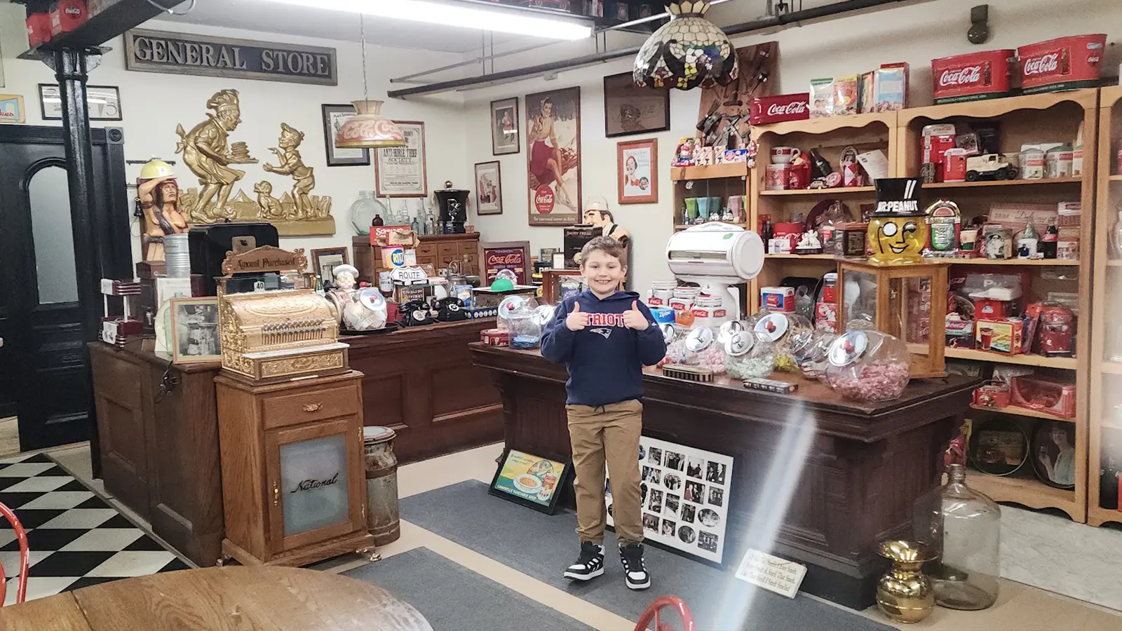 The antique general store inside the Automotion Garage, with a vintage brass cash register, penny candy jars on a wooden counter, and shelves of Coca-Cola memorabilia.