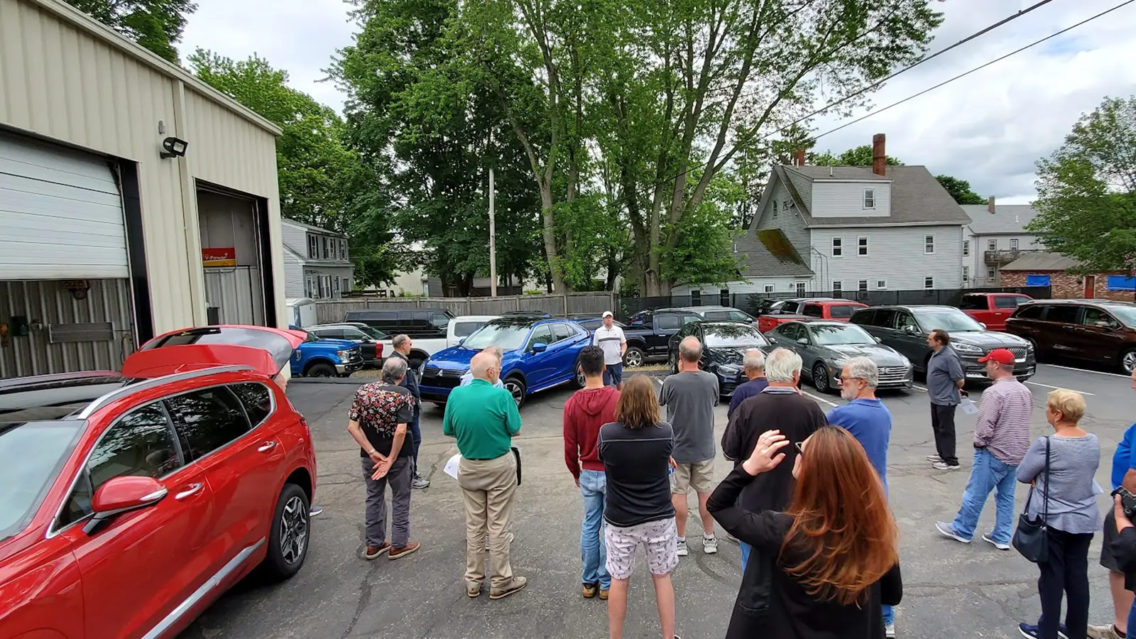 NEMPA members gather outside the Automotion Garage in Middleborough for a walkaround presentation, with press vehicles including Hyundai and Mitsubishi models staged in the parking lot.
