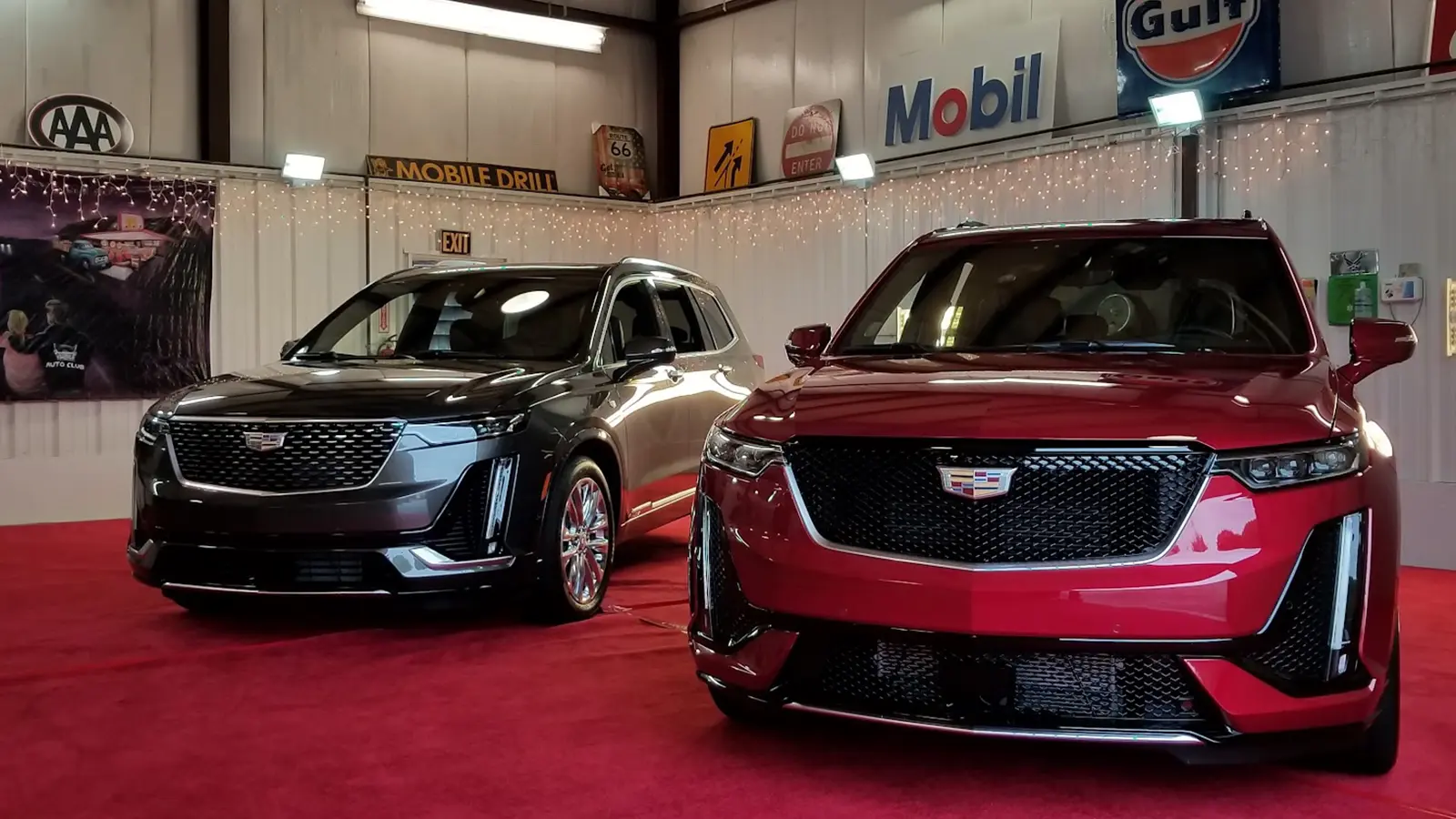 Two Cadillac XT6 crossovers displayed on red carpet inside the Automotion Garage, surrounded by vintage Gulf, Mobil, and AAA signs